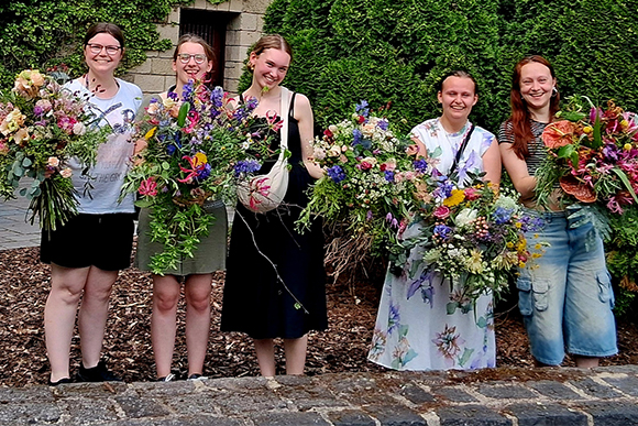 Fünf junge Frauen, lachend, mit großen Blumensträußen in den Händen